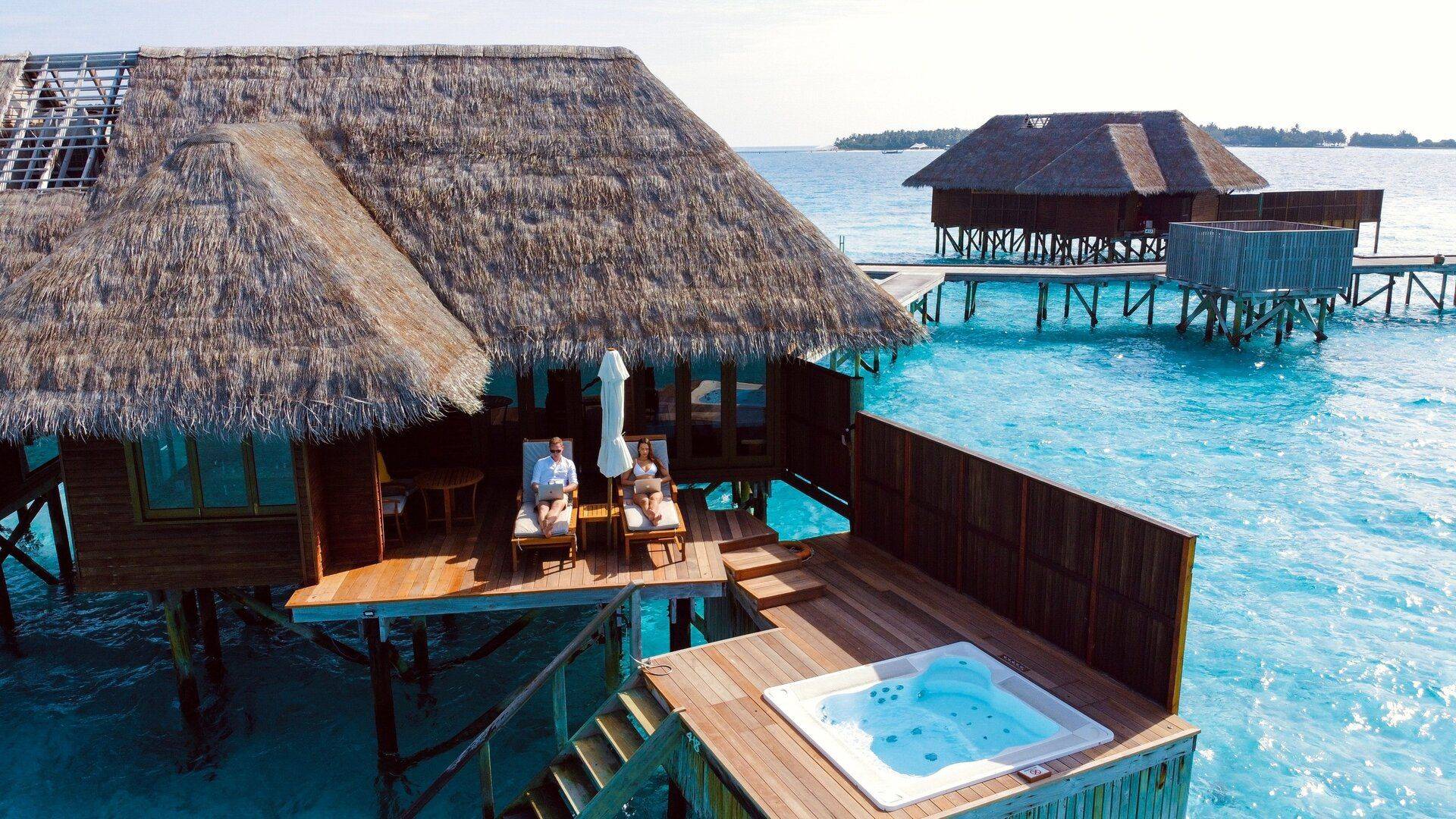 two digital nomads lounge chairs typing on laptops outside maldives vacation home