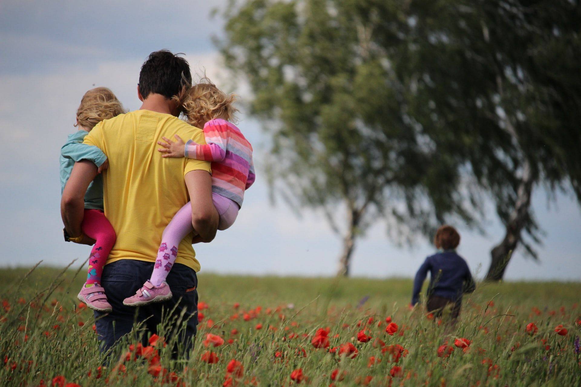 man carrying daughters in meadow of red flowers