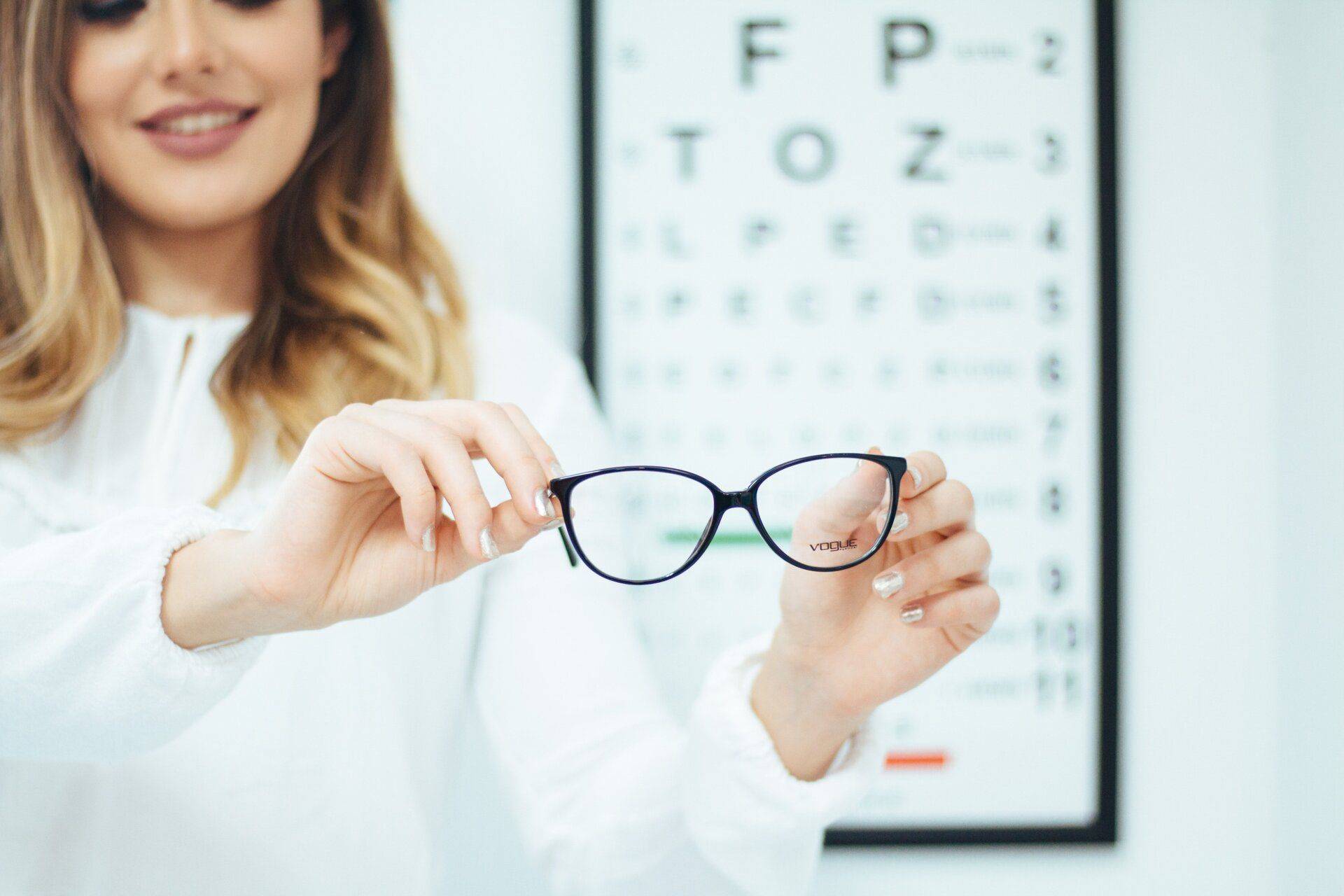woman holding up a pair of glasses in front of an eye chart