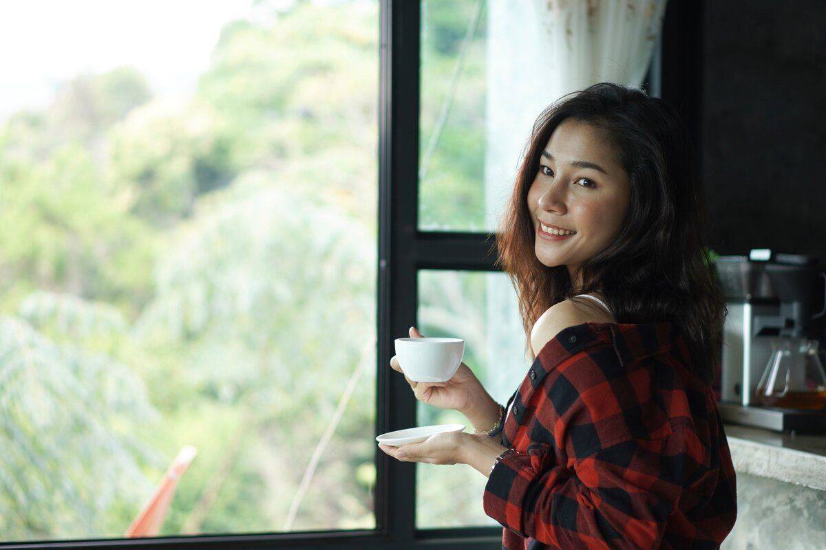asian woman relaxing with a cup of coffee by the window