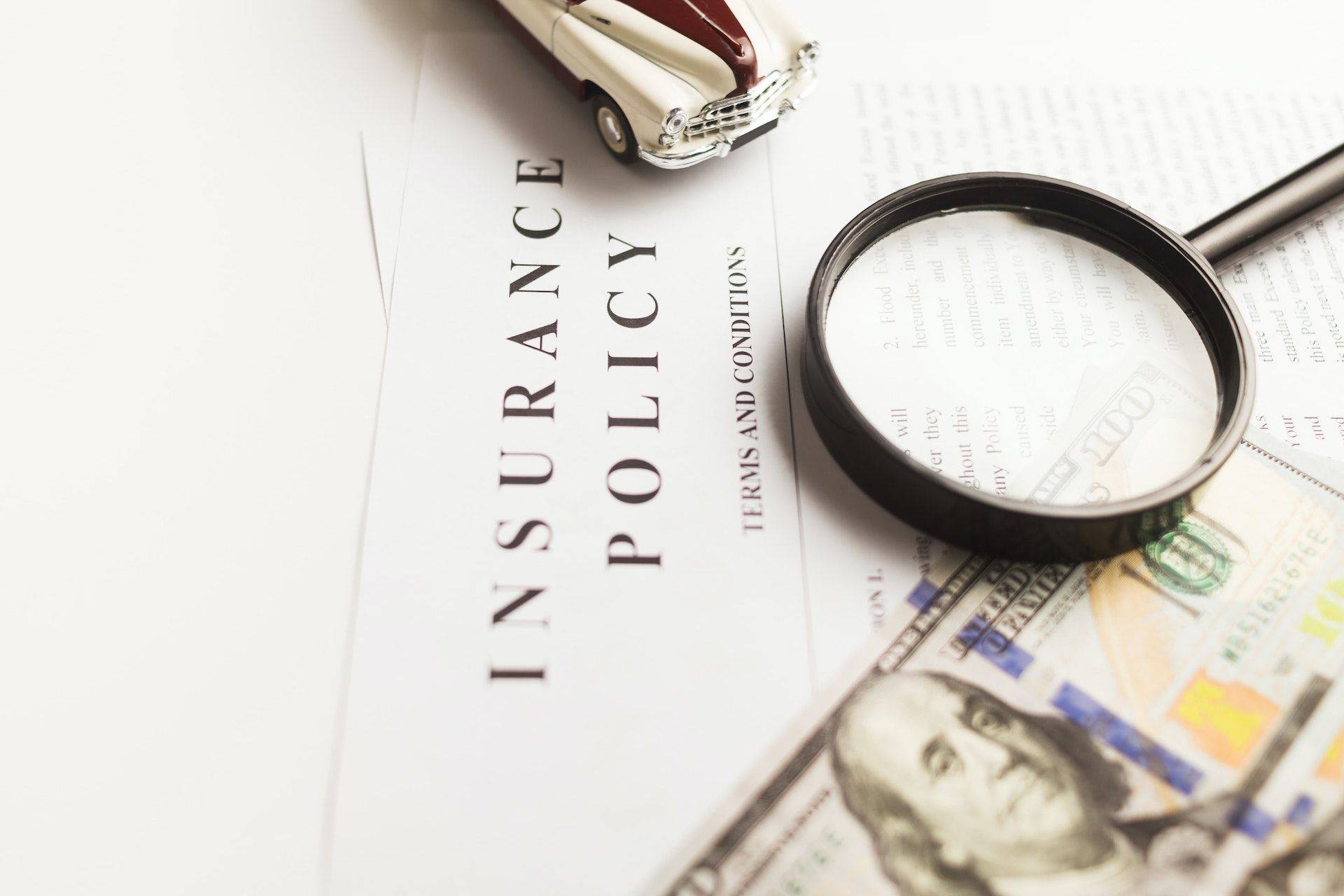 printed insurance policy with magnifying glass and US hundred-dollar bills